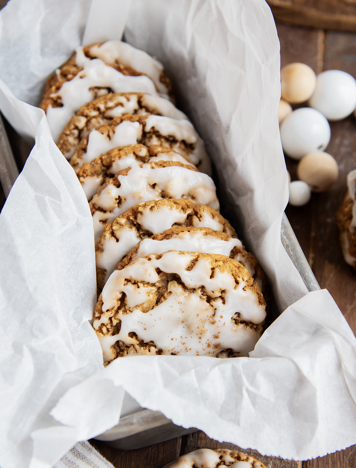 A side ways stack of iced gingerbread oatmeal cookies in a parchment paper lined tin.
