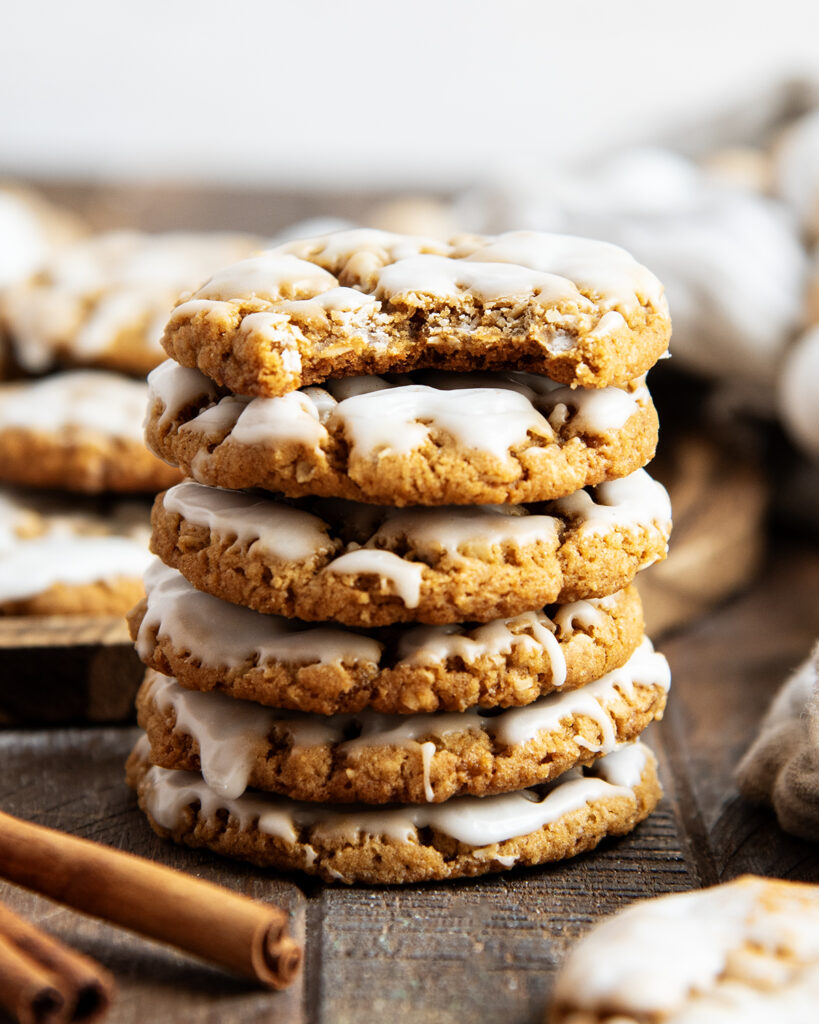 A stack of gingerbread oatmeal cookies, with icing on top, and the top cookies has a bite out of it.
