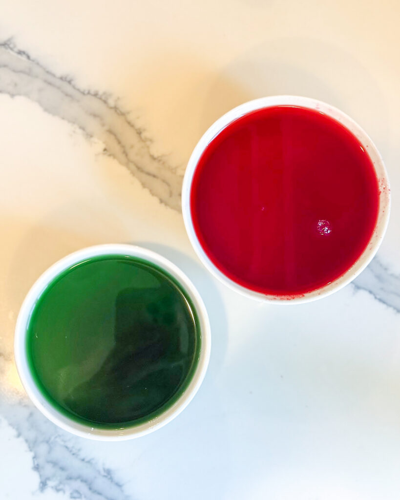 Two small bowls of liquid jello, one is green and one is red.