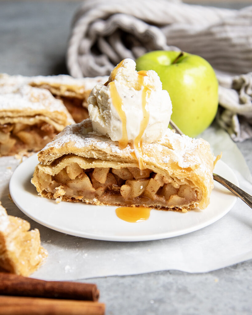 A slice of German Apple Strudel on a plate with vanilla ice cream on top.
