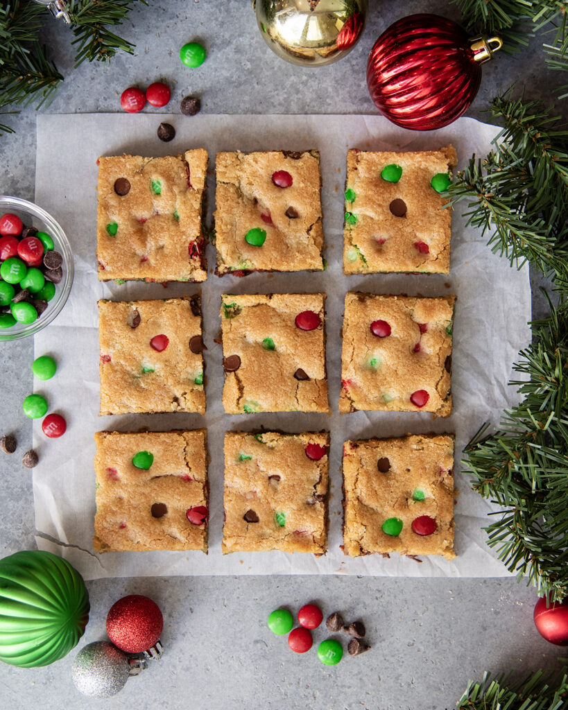 An above view of christmas m&m cookie bars in rows on a piece of parchment paper. 