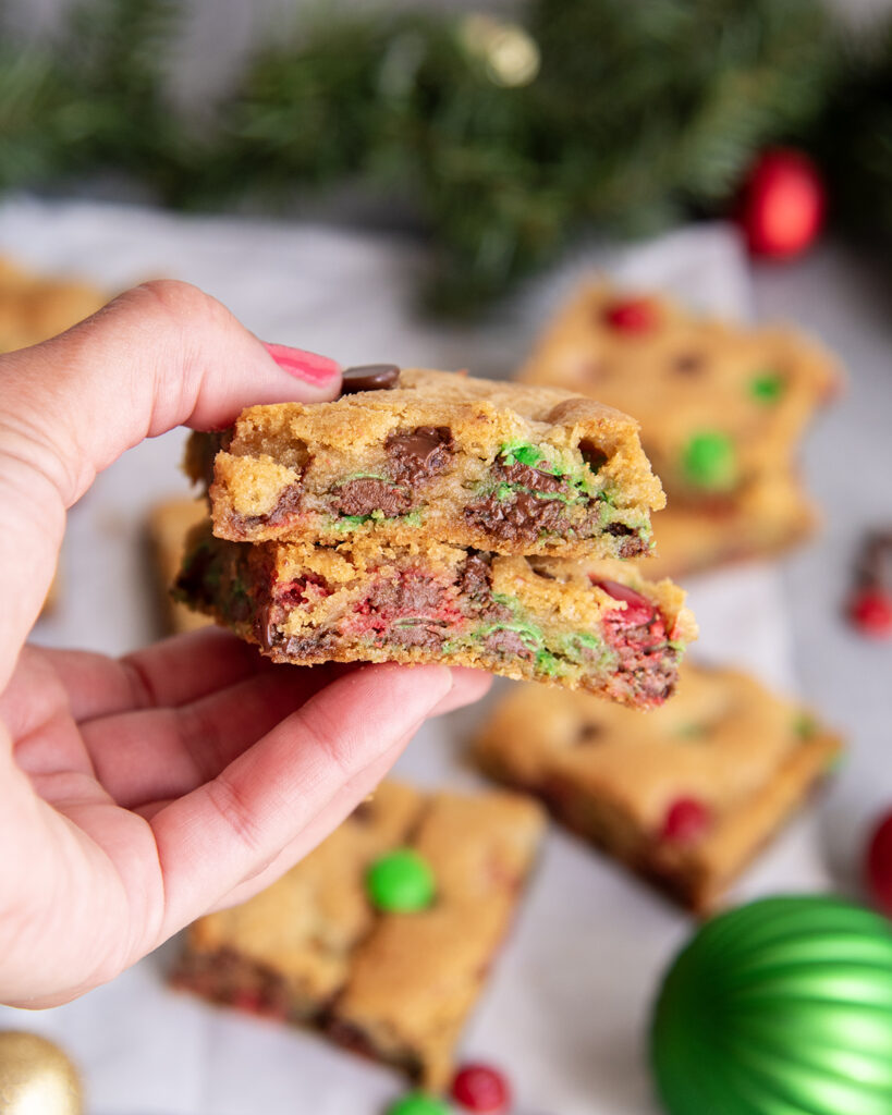 A hand holding two christmas M&M cookie bars.