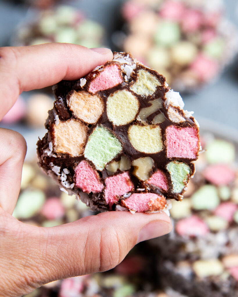 A hand holding a Church Window candy filled with colorful mini marshmallows, and walnuts coated in chocolate and coconut.