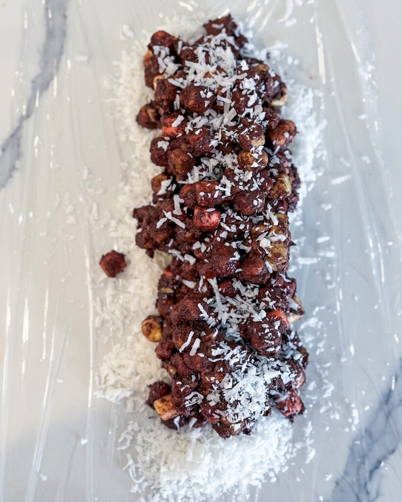 Mini marshmallows coated in chocolate spread out in a rectangle on coconut.