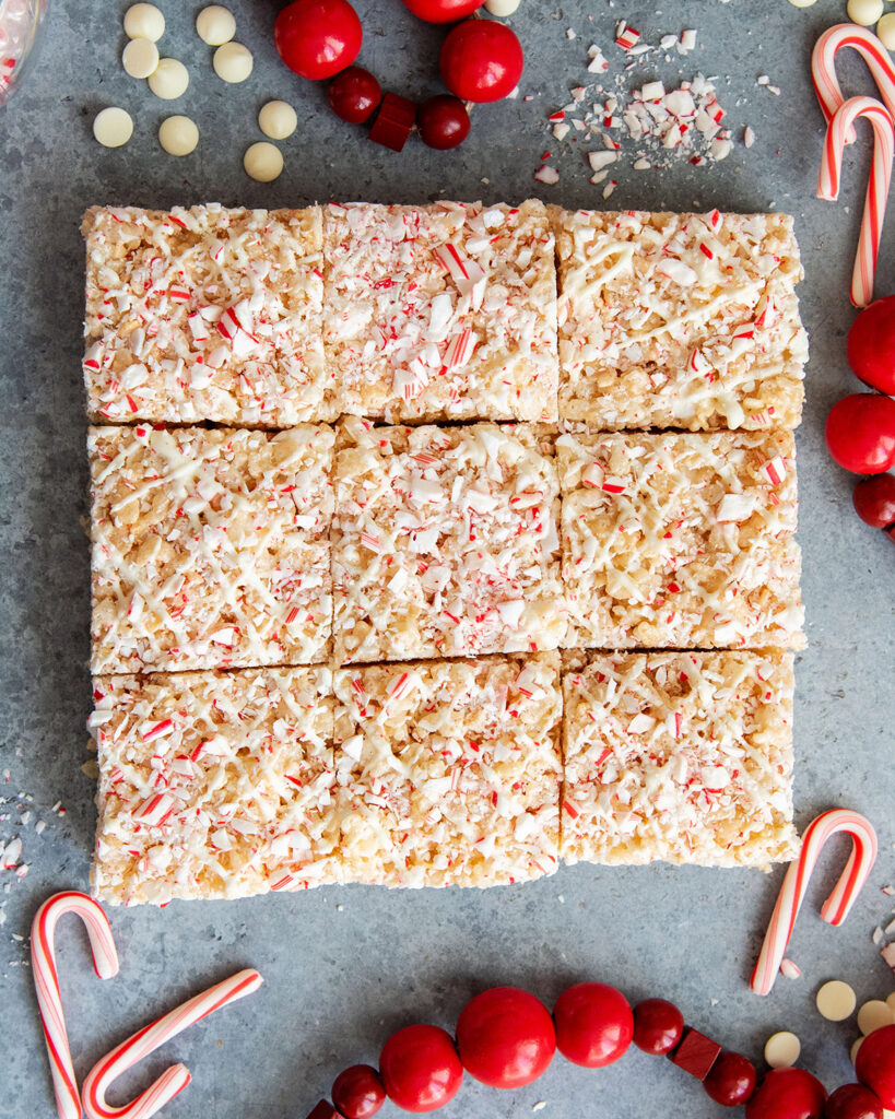 Peppermint rice krispie treat squares squished together on a counter top, and surrounded by candy cane pieces.