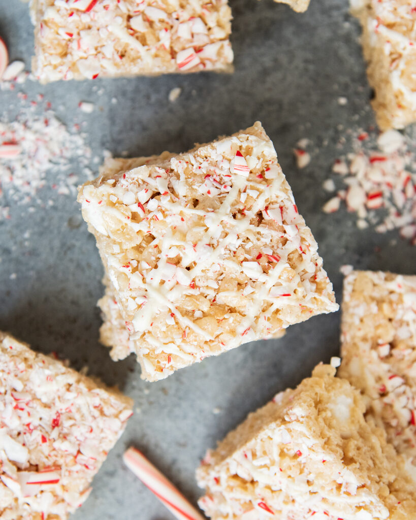 An above view of a stack of rice krispie treats topped with white chocolate drizzles and peppermint candy pieces.