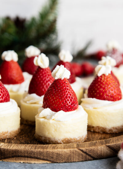 A wooden serving plate topped with mini cheesecakes with a strawberry on top.