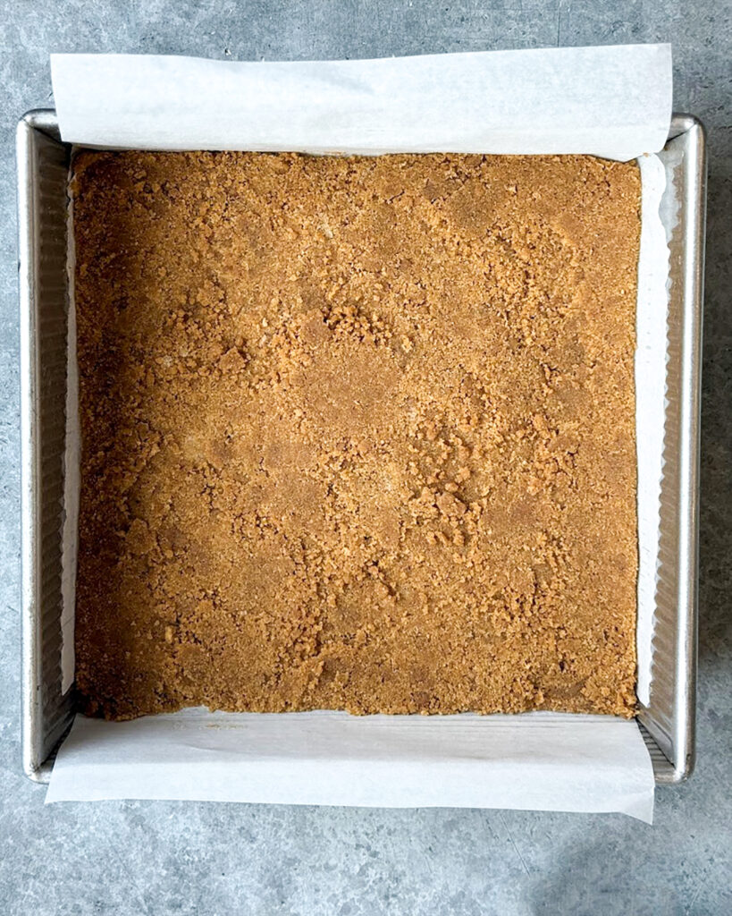 A graham cracker crust in a square pan.