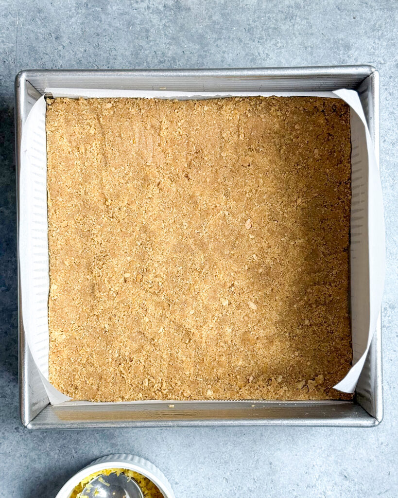 A graham cracker crust in a square pan.