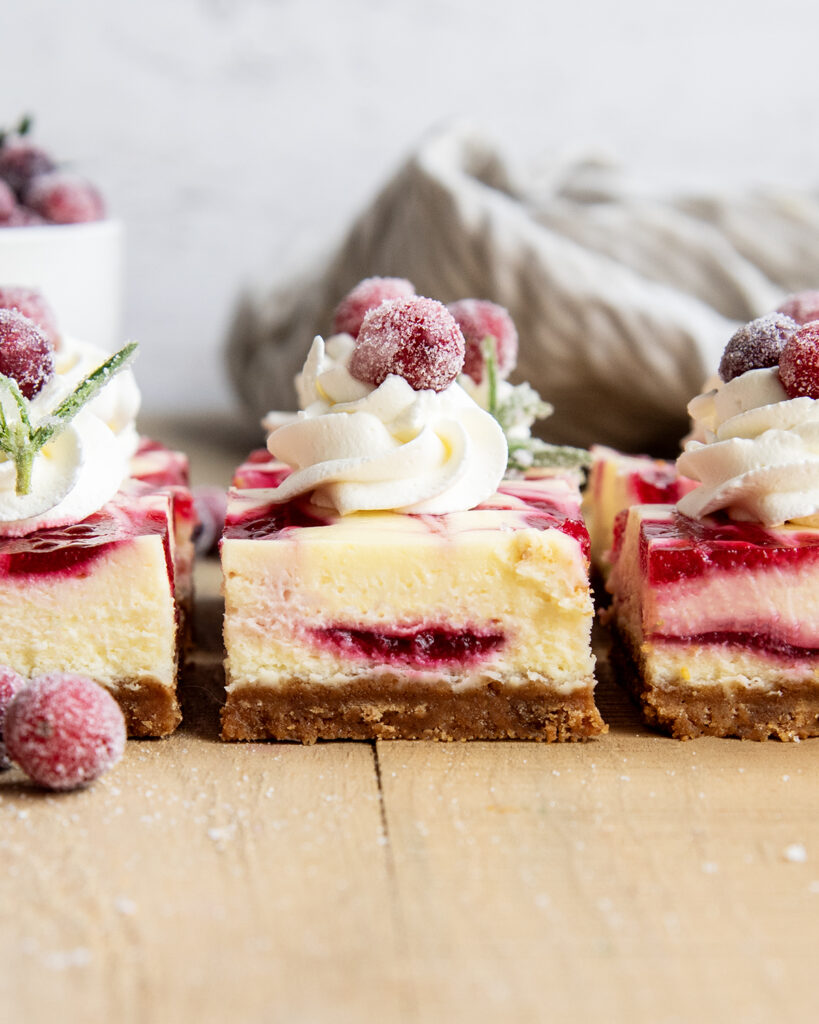 A side view of cranberry cheesecake bars topped with whipped cream.