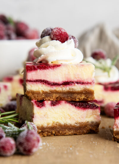A stack of two pieces of cranberry cheesecake with cranberry sauce swirled throughout, and the top is topped with whipped cream and a candied cranberry.