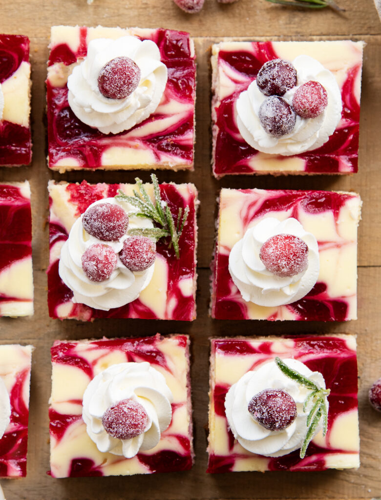 An above view of squares of creanberry cheesecake bars topped with whipped cream.