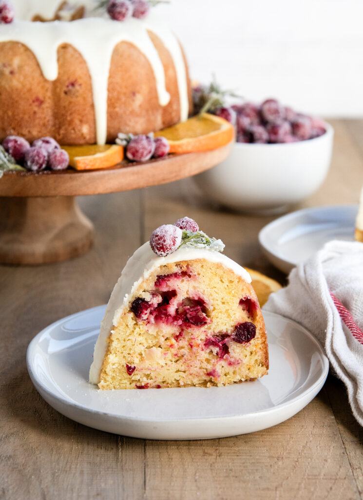 A slice of cranberry orange bundt cake on a plate, topped with a vanilla glaze.