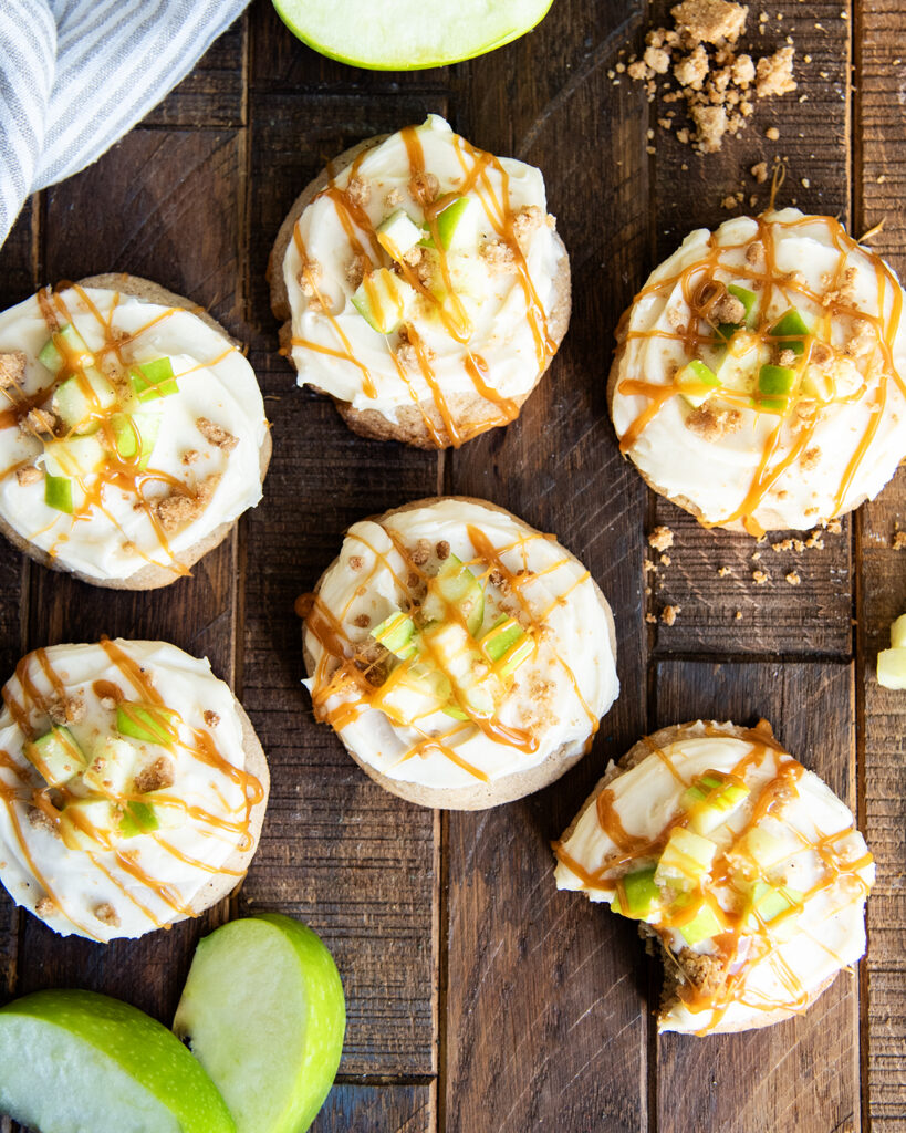An above view of caramel apple cookies topped with apple pieces, caramel, and streusel topping.
