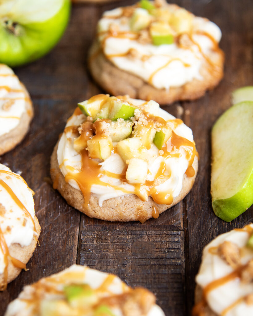 A copycat Crumbl Caramel Apple cookie topped with caramel cream cheese frosting and apple pieces.