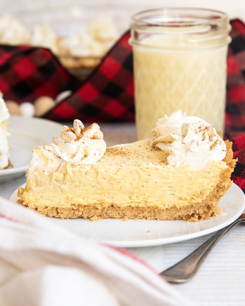 A white plate with a slice of eggnog pie topped with whipped cream on top.