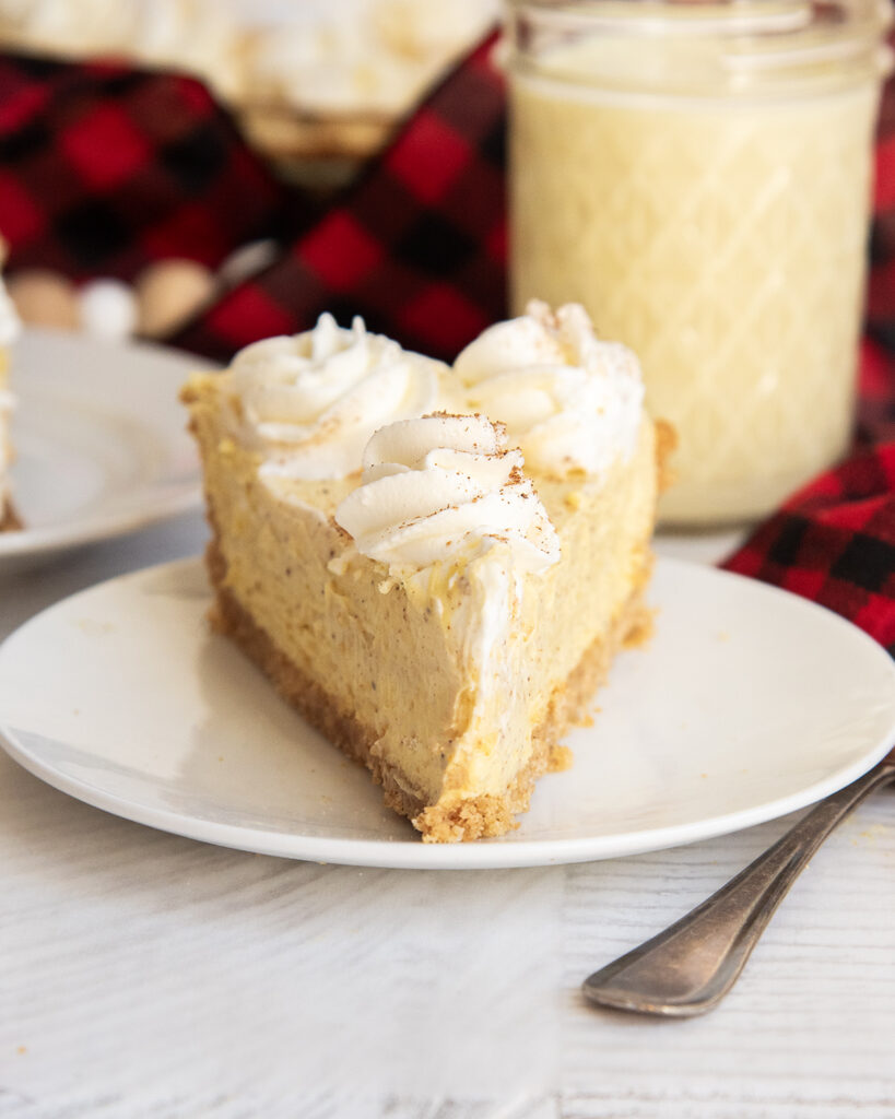 A white plate with a slice of eggnog pie topped with whipped cream on top.
