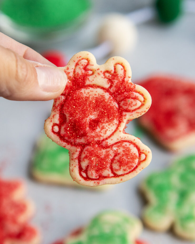 A hand holding a red sugar topped reindeer shortbread cookie.