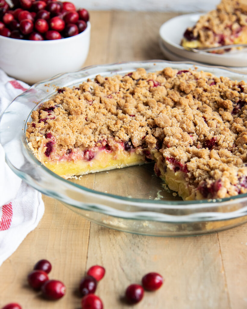 A Custard pie with cranberries and a streusel topping in a glass pie dish.
