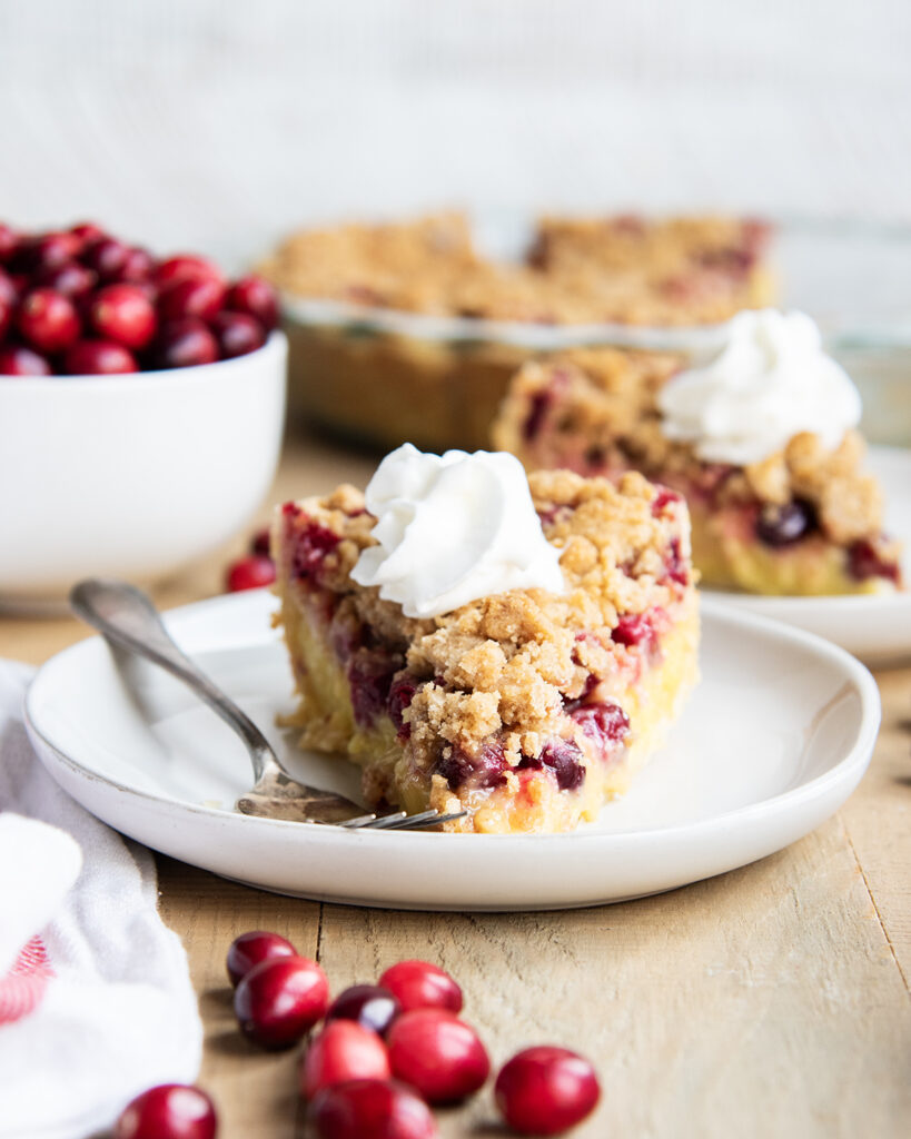 A slice of cranberry custard pie, with a crumb topping and whipped cream on top.