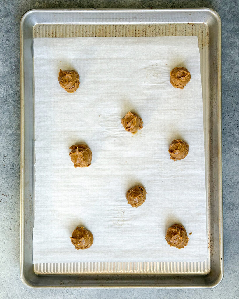 Scoops of gingerbread whoopie pie cookie batter on a cookie sheet.