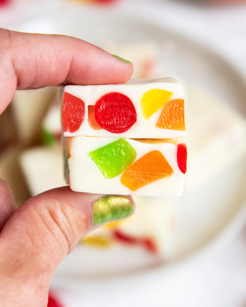 A hand holding two gumdrop filled nougat candies.