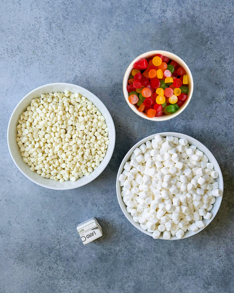The ingredients needed to make homemade gumdrop nougat, with white chocolate, marshmallows, gumdrops, and butter.