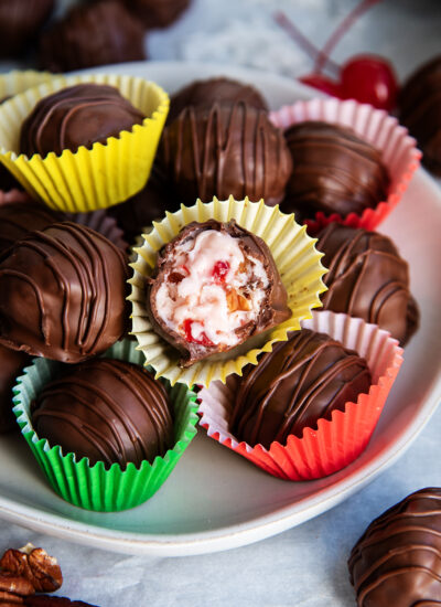 A plate of Martha Washington Balls in candy wrappers, one is cut open showing the pink coconut and cherry filling.
