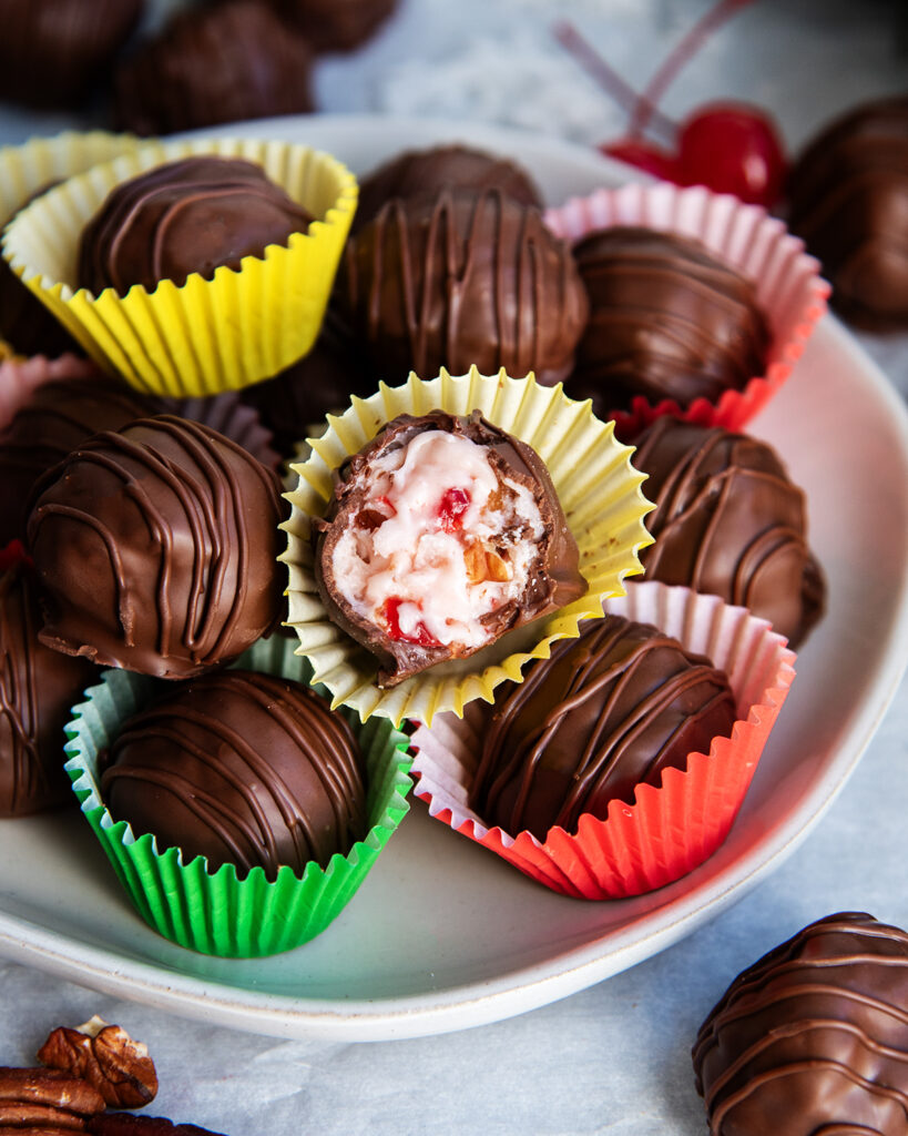 A plate of Martha Washington Balls in candy wrappers, one is cut open showing the pink coconut and cherry filling.