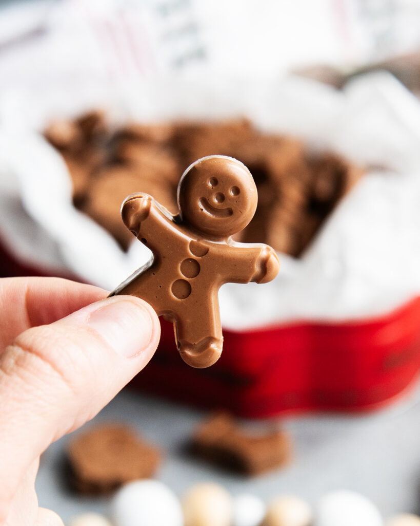 A hand holding a gingerbread man shaped peanut butter meltaway.