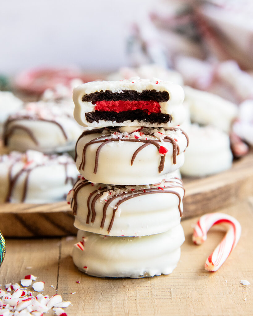 A stack of four white chocolate peppermint covered oreos, and the top has a bite out of it showing a red Oreo creme center.