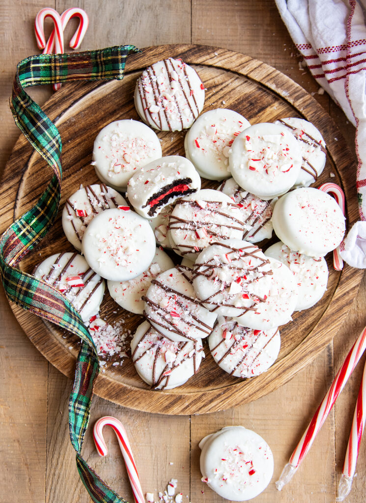An above view of peppermint bark white chocolate Oreos in a pile on a wooden board.
