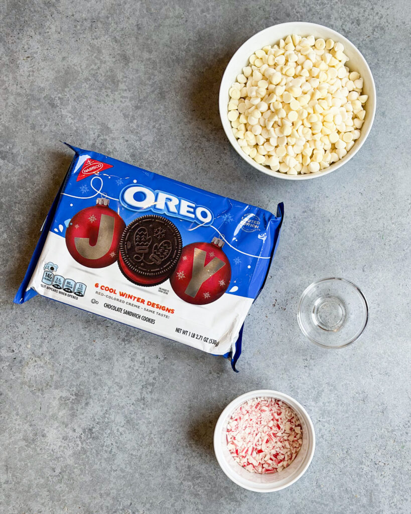 Ingredients needed to make peppermint bark Oreos, including Oreos, white chocolate, candy cane pieces and peppermint extract. 