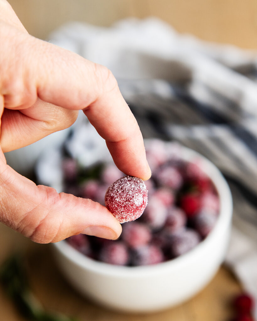 A sugared cranberry held between two fingers.