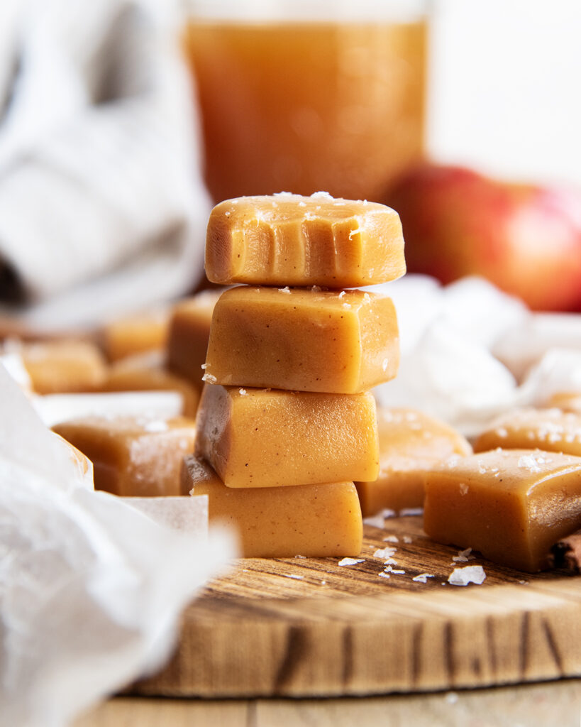 A stack of four apple cider caramels on a wooden board. The top one has a bite out of it.