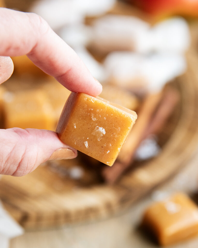 Two fingers holding an apple cider caramel topped with sea salt.