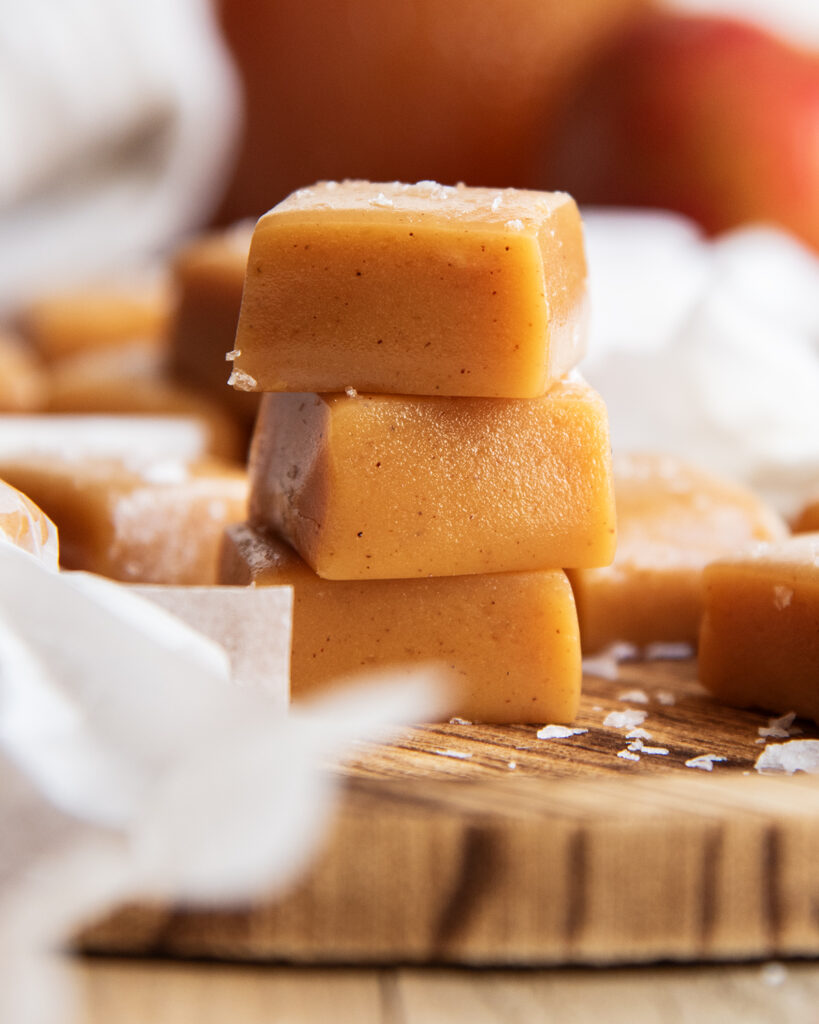A stack of three apple cider caramels on a wooden board.
