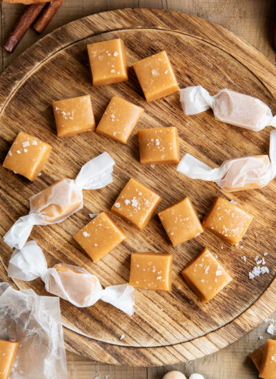 Apple cider caramels on a wooden tray, some are wrapped in parchment paper.
