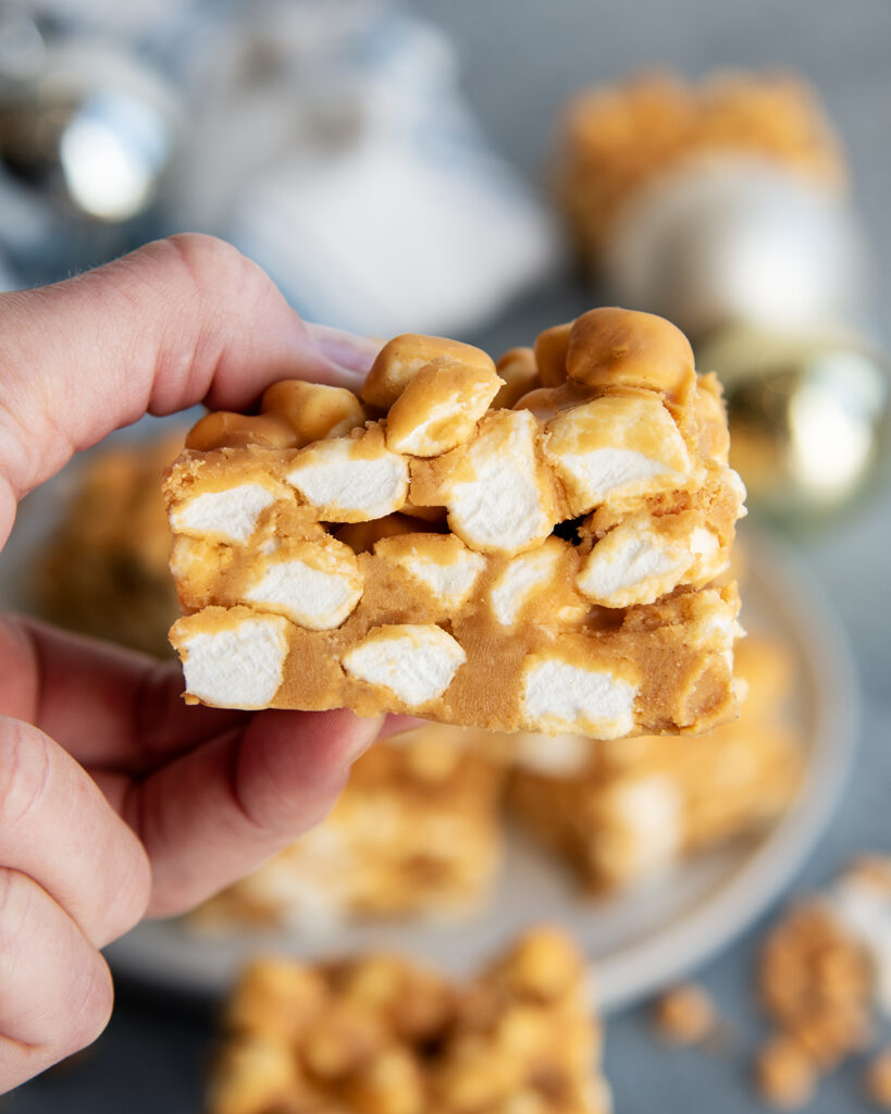 A hand holding a peanut butter butterscotch marshmallow square.