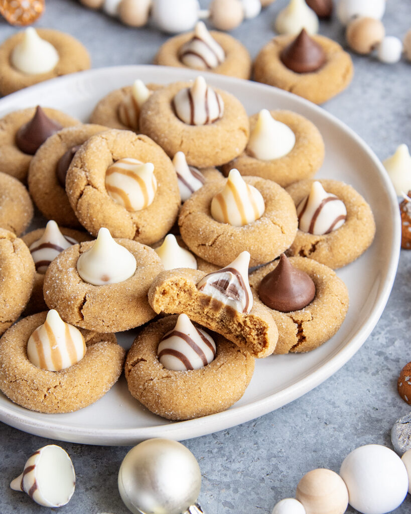 A plate of ginger blossom cookies, with kisses and hugs candies on top. One cookie has a bite out of it.