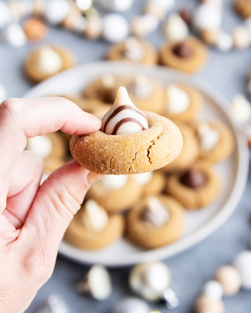A hand holding a ginger blossom cookies with a Hershey Hug on top.