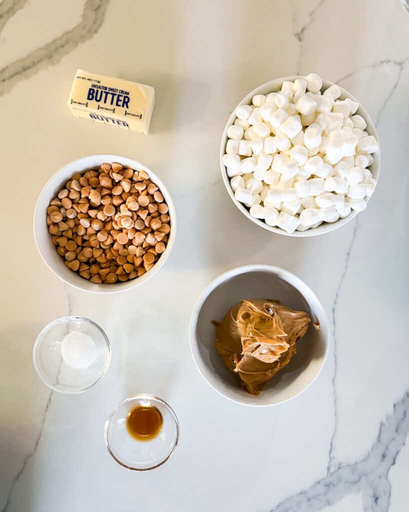 The ingredients needed to make peanut butter marshmallow squares all in small bowls, including marshmallows, butterscotch chips, peanut butter, and butter.