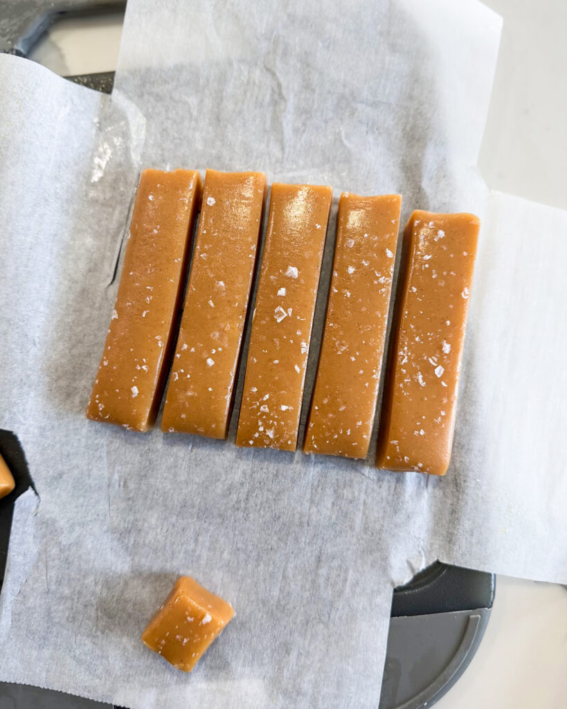 Sliced caramels on parchment paper topped with flakey salt.