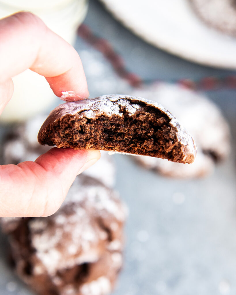 A hand holding a chocolate cake mix crinkle cookie with a bite out of it.
