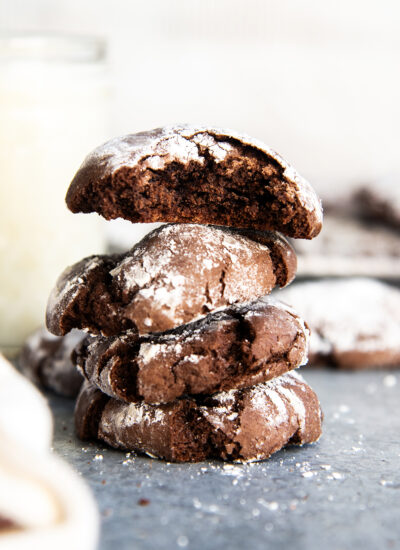 A stack of four chocolate cake mix crinkle cookies coated in powdered sugar. The top cookie has a bite out of it.