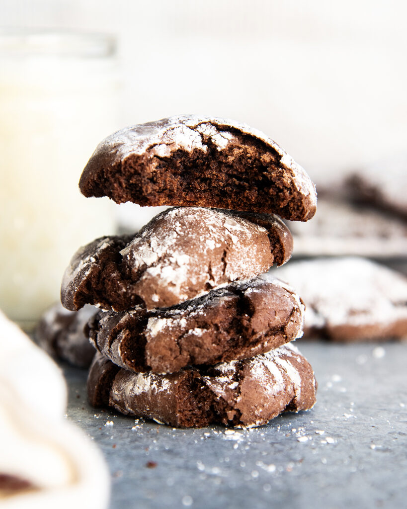 A stack of four chocolate cake mix crinkle cookies coated in powdered sugar. The top cookie has a bite out of it.