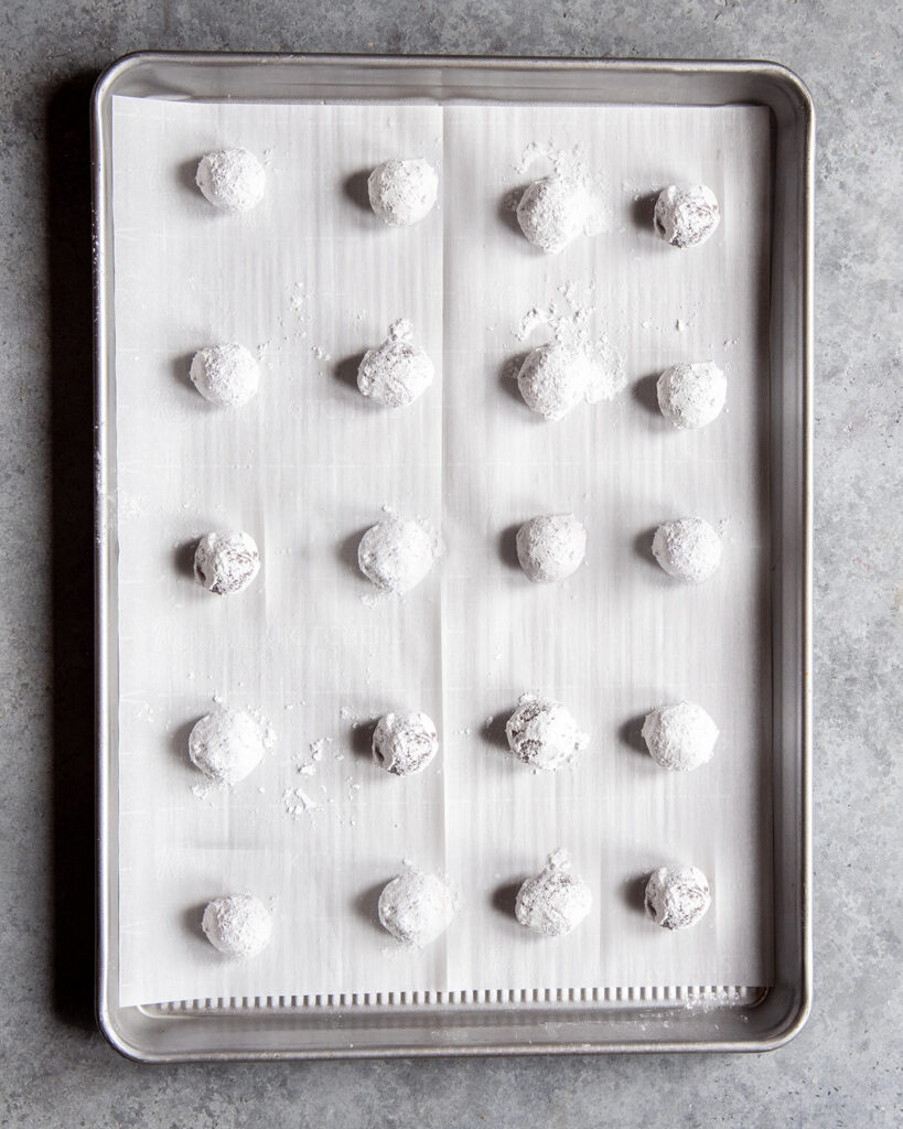 A cookie sheet with balls of chocolate cookie dough rolled in powdered sugar. 
