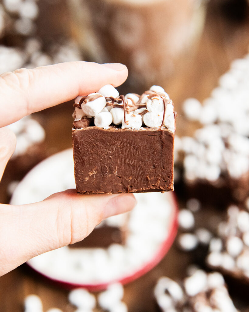 A hand holding a piece of hot chocolate fudge topped with mini marshmallows.