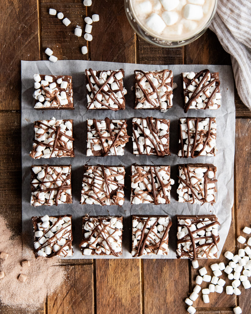 Rows of hot chocolate fudge pieces, each piece of chocolate fudge is topped with dehydrated marshmallows and a drizzle of chocolate.