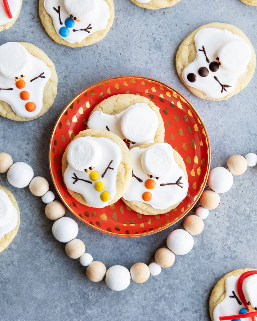 A plate of three melted snowman cookies decorated with royal icing and marshmallows.